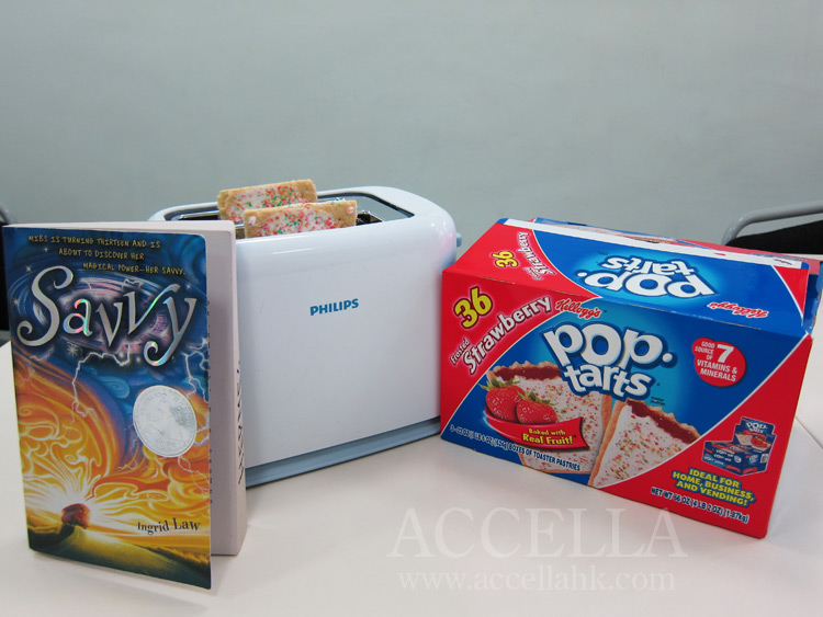 Left to right: paperback copy of savvy, toaster loaded with two strawberry Pop-Tarts, box of strawberry Pop-Tarts.